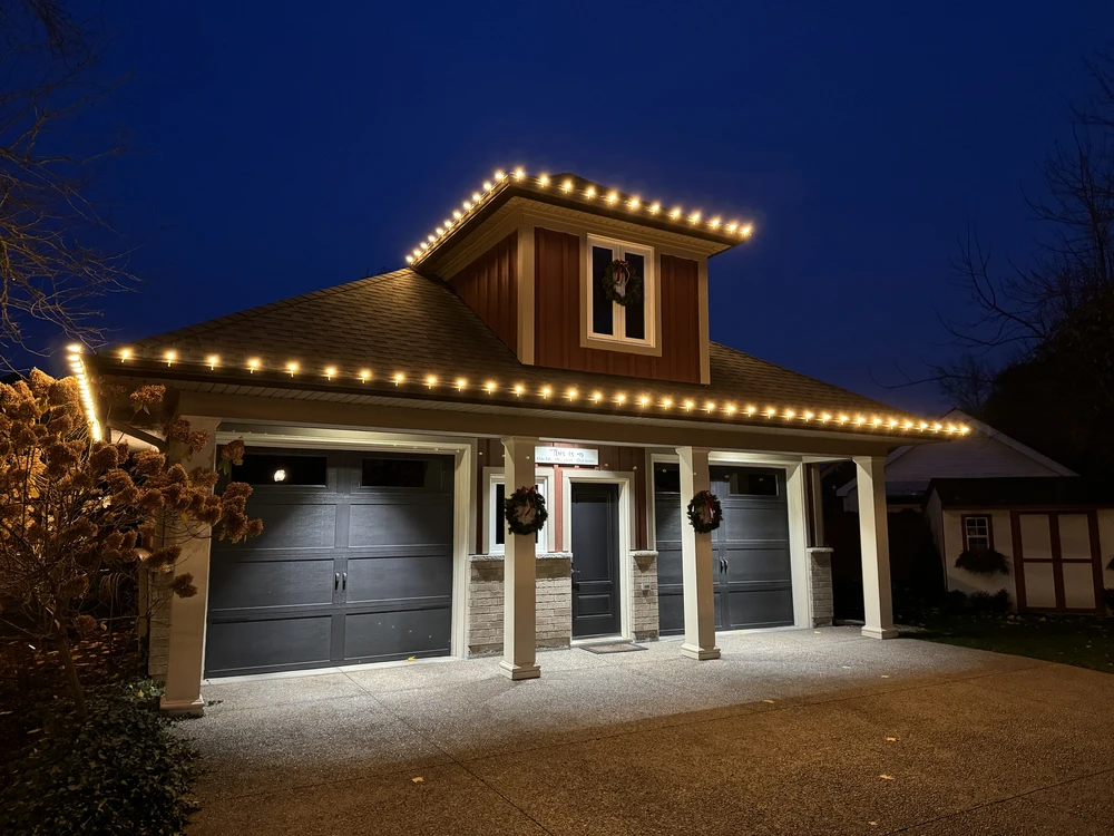 Professional Christmas lights installation featuring warm white C9 bulbs outlining the roofline of a modern home with a double garage at night.