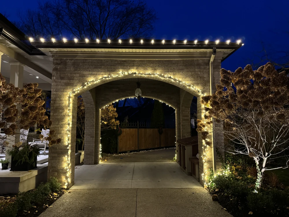 Detailed holiday light installation showing warm white mini lights elegantly wrapped around a custom brick archway for a festive entryway.