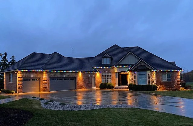 A sprawling brick home at dusk with professional light installations of multi-colored bulbs tracing the entire roofline.